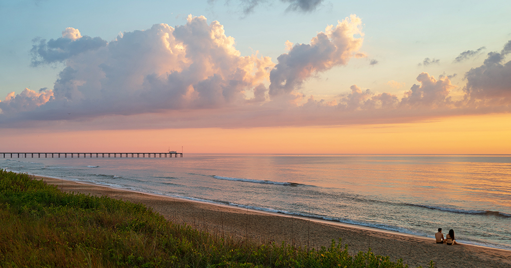 A couple enjoying the beach with Duck Research Pier in the distance