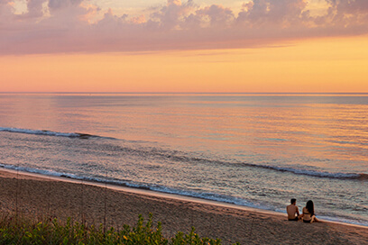 a couple sitting on an Outer Banks beach watching the sunset